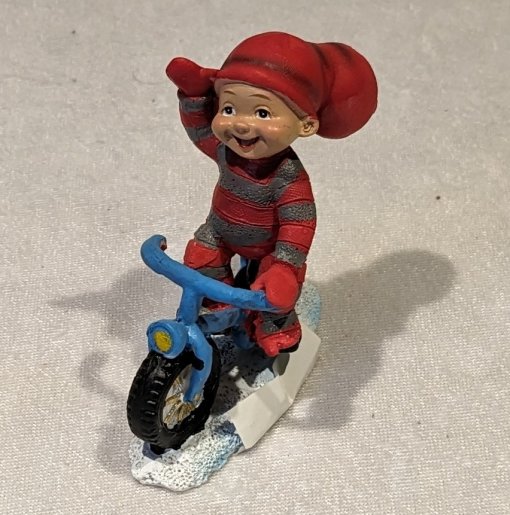 Baby-Elf-Junge winkt, während er ein blaues Fahrrad fährt